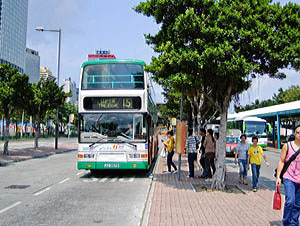 People wait under the trees outside the central ferry pier as they wait for bus 15 to The Peak