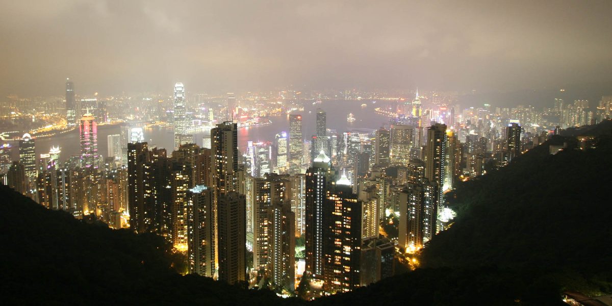 The Peak Tower at night, its overhanging wok-shaped roof lit by warm architectural lights, seen from below