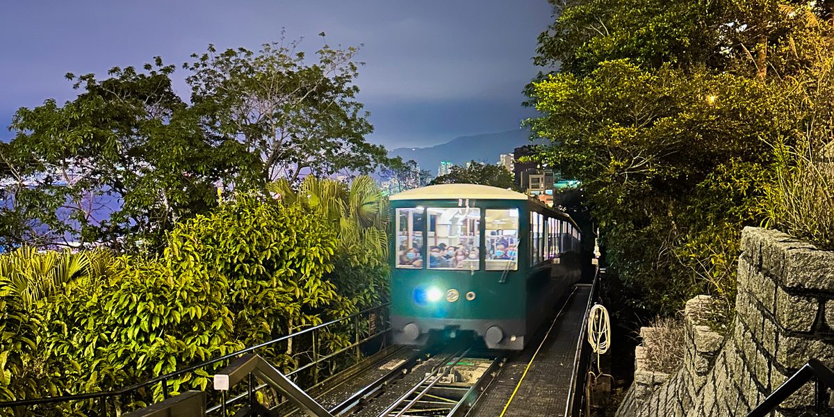 A Peak Tram car on the steep twin-rail track after dark, with city lights behind it
